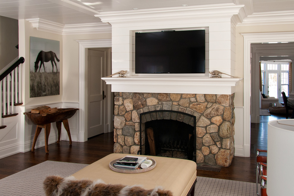 Стильный дизайн: открытая гостиная комната среднего размера в стиле кантри с бежевыми стенами, темным паркетным полом, стандартным камином, фасадом камина из камня и телевизором на стене - последний тренд