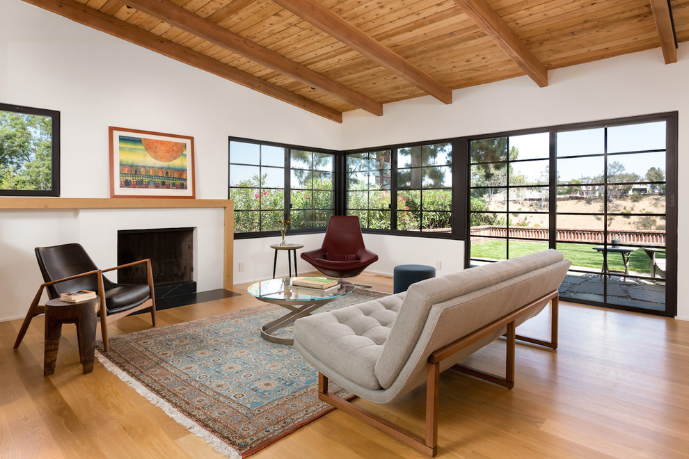 Mittelgroßes, Fernseherloses Retro Wohnzimmer mit weißer Wandfarbe, hellem Holzboden, Kamin und verputzter Kaminumrandung in Los Angeles