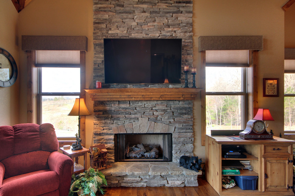 アトランタにある中くらいなトラディショナルスタイルのおしゃれなリビング (ベージュの壁、無垢フローリング、吊り下げ式暖炉、石材の暖炉まわり、壁掛け型テレビ) の写真