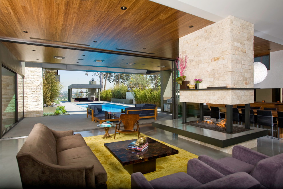 ロサンゼルスにあるコンテンポラリースタイルのおしゃれなリビング (コンクリートの床、両方向型暖炉、石材の暖炉まわり、茶色いソファ) の写真