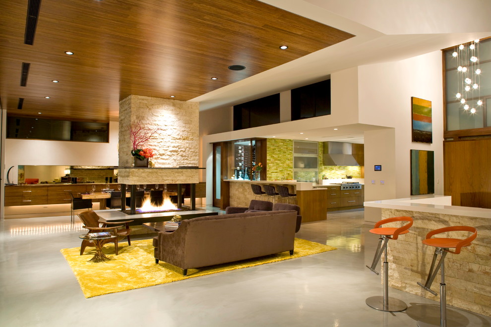 На фото: гостиная комната в современном стиле с домашним баром, бетонным полом, двусторонним камином, фасадом камина из камня и коричневым диваном