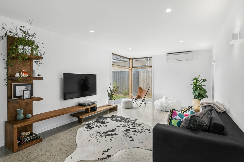 Mittelgroßes, Offenes Modernes Wohnzimmer mit weißer Wandfarbe, Betonboden, Kaminumrandung aus Beton, TV-Wand und grauem Boden in Geelong