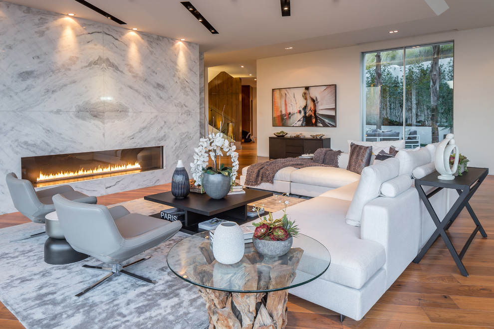 Modernes Wohnzimmer mit weißer Wandfarbe, braunem Holzboden, Gaskamin, Kaminumrandung aus Stein und braunem Boden in Los Angeles