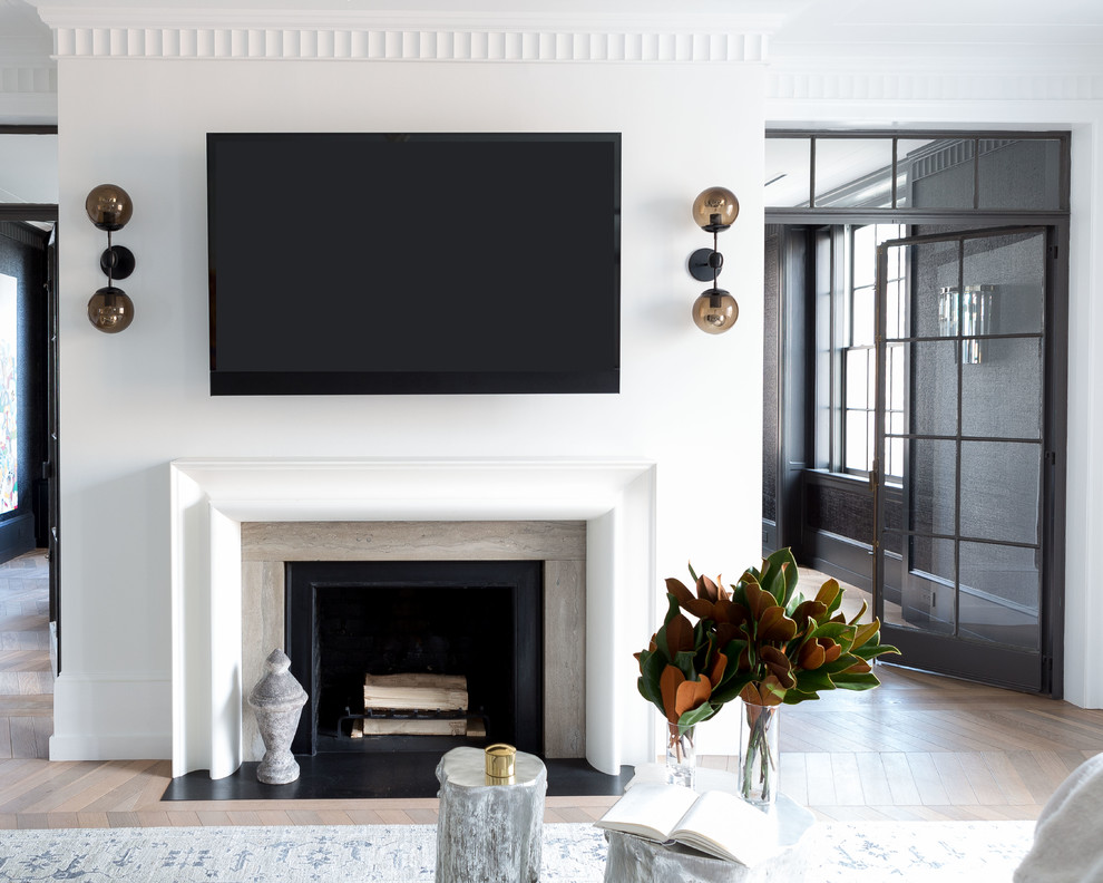 Источник вдохновения для домашнего уюта: гостиная комната в стиле неоклассика (современная классика) с белыми стенами, светлым паркетным полом, стандартным камином, фасадом камина из камня, телевизором на стене и коричневым полом