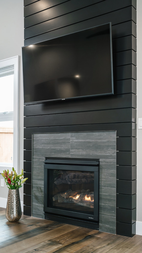 Свежая идея для дизайна: гостиная комната среднего размера в стиле неоклассика (современная классика) с черными стенами, стандартным камином, фасадом камина из дерева, телевизором на стене и черным полом - отличное фото интерьера