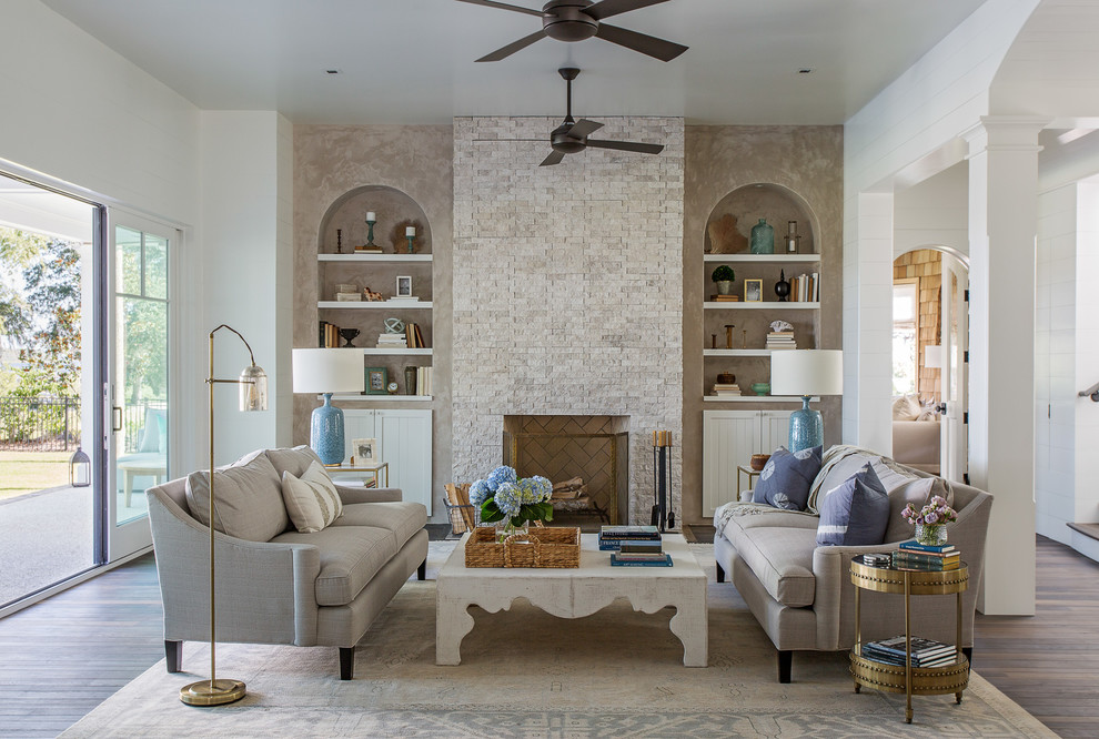 Maritimes Wohnzimmer mit weißer Wandfarbe, braunem Holzboden, Kamin, Kaminumrandung aus Stein und braunem Boden in Charleston