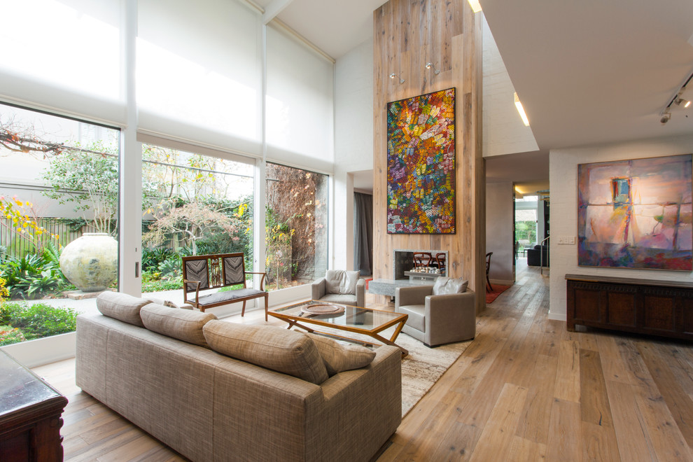 Offenes Modernes Wohnzimmer mit weißer Wandfarbe, braunem Holzboden, Tunnelkamin und Kaminumrandung aus Holz in Orange County