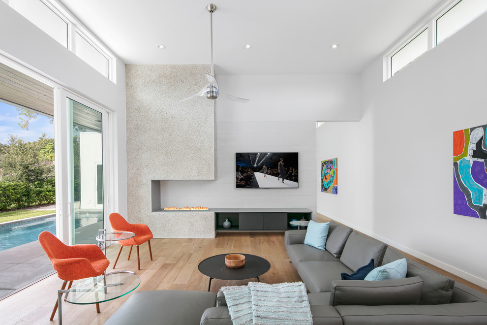 Modern inredning av ett mellanstort allrum med öppen planlösning, med vita väggar, ljust trägolv, en bred öppen spis, en spiselkrans i betong, en väggmonterad TV och brunt golv