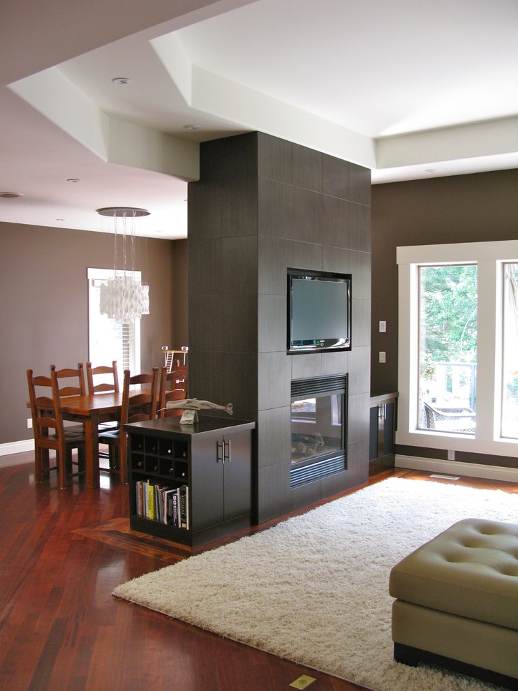 Modern inredning av ett stort allrum med öppen planlösning, med bruna väggar, mellanmörkt trägolv, en dubbelsidig öppen spis, en spiselkrans i trä och en väggmonterad TV