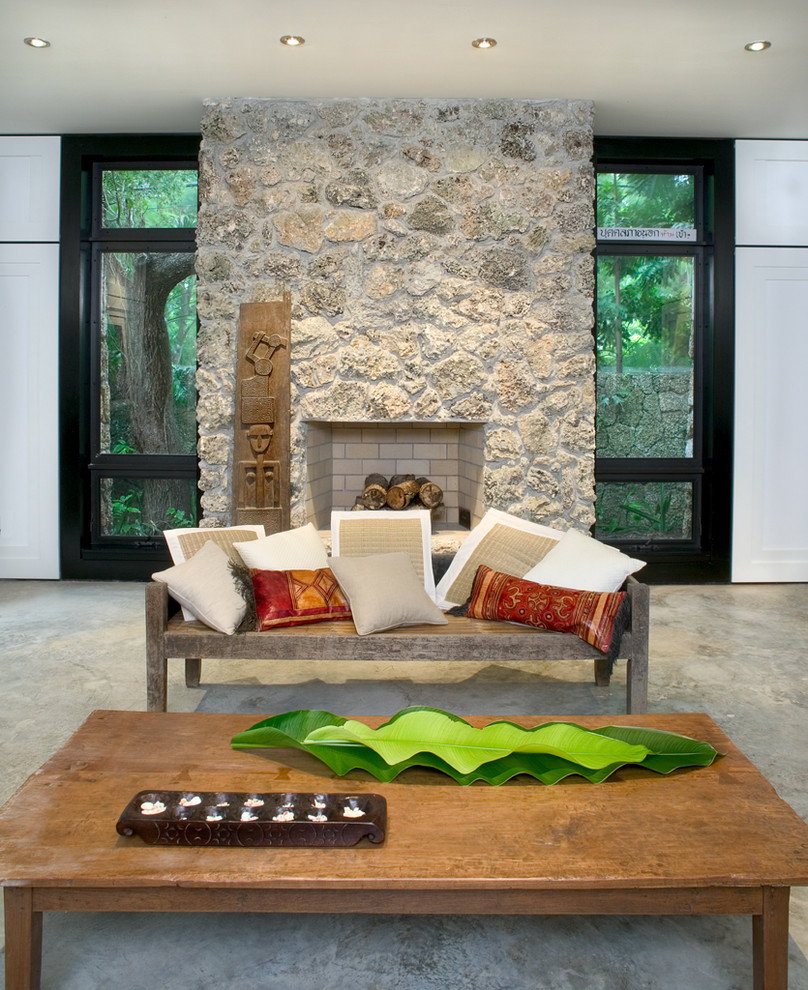 マイアミにある高級な広いトロピカルスタイルのおしゃれなリビング (ベージュの壁、コンクリートの床、標準型暖炉、石材の暖炉まわり、テレビなし、グレーの床) の写真
