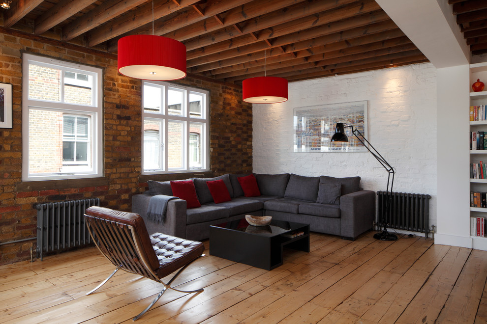 Large industrial open plan living room in London with white walls, light hardwood flooring, no fireplace, no tv, brown floors, exposed beams and brick walls.