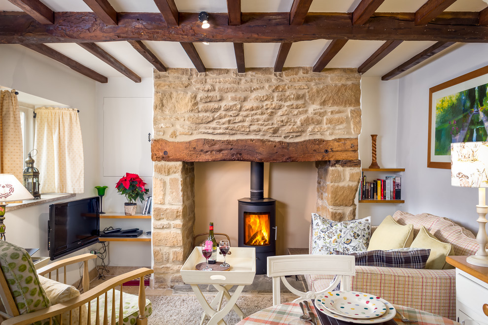 Kleines, Abgetrenntes Landhaus Wohnzimmer mit weißer Wandfarbe, Kaminofen, freistehendem TV, Teppichboden, Kaminumrandung aus Stein und Steinwänden in Gloucestershire