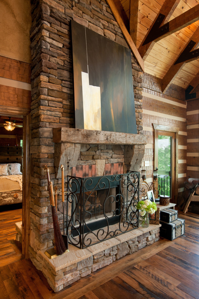 Foto de salón abierto rural grande con paredes marrones, suelo de madera en tonos medios, chimenea de doble cara y marco de chimenea de piedra