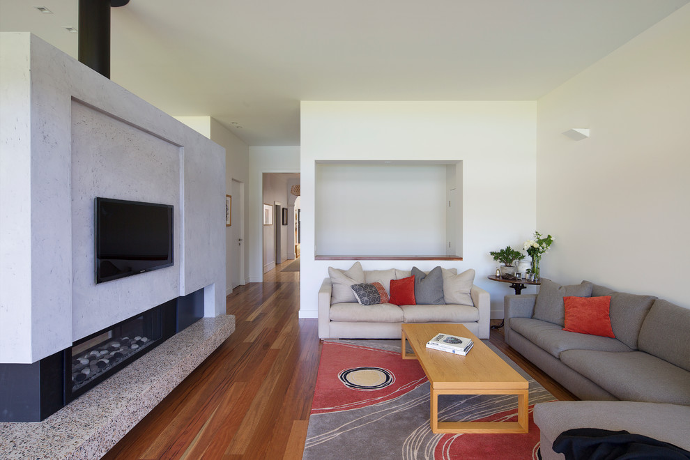 Modelo de salón contemporáneo con paredes blancas, suelo de madera en tonos medios, chimenea de doble cara y televisor colgado en la pared