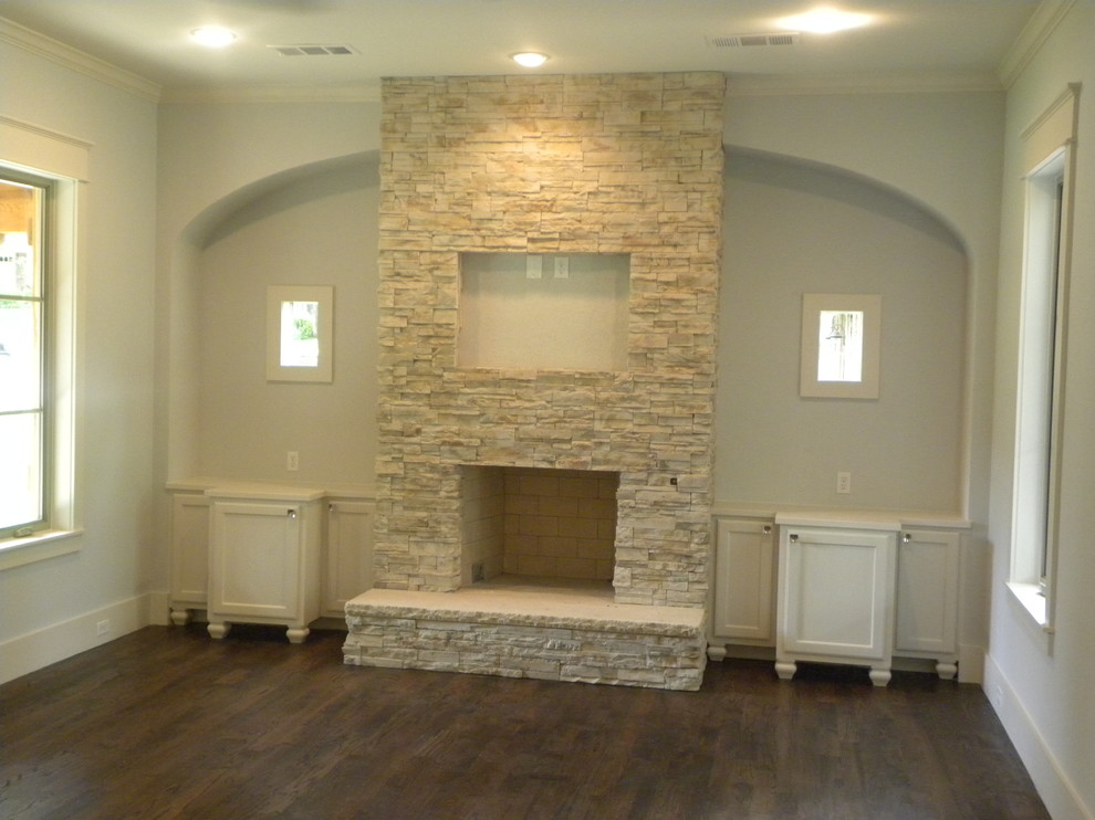 Cette photo montre un salon craftsman ouvert avec une salle de réception, un mur gris, un sol en bois brun, une cheminée standard, un manteau de cheminée en pierre et un téléviseur fixé au mur.