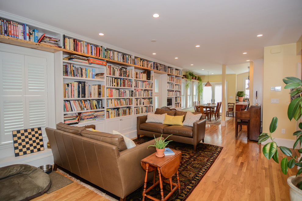 Foto de biblioteca en casa abierta rural de tamaño medio con paredes amarillas, suelo de madera en tonos medios, marco de chimenea de madera y televisor colgado en la pared