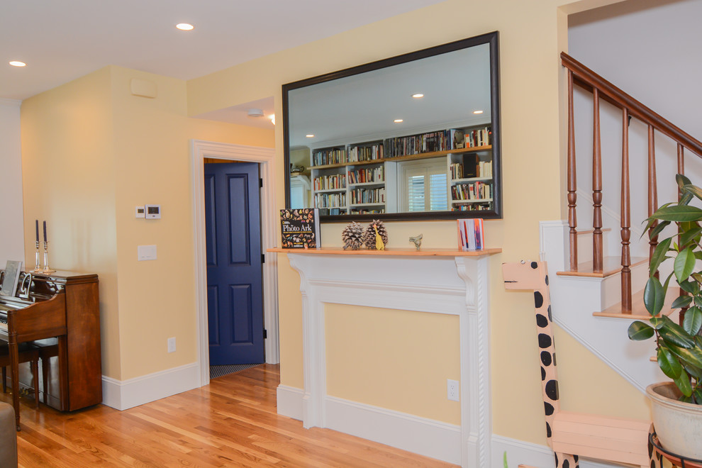 Immagine di un soggiorno rustico di medie dimensioni e aperto con libreria, pareti gialle, pavimento in legno massello medio, cornice del camino in legno e TV a parete