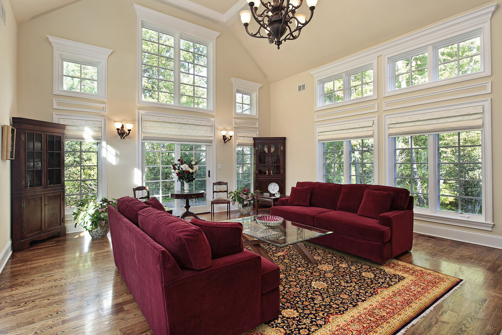 Пример оригинального дизайна: большая парадная, открытая гостиная комната в классическом стиле с паркетным полом среднего тона, бежевыми стенами и бордовым диваном