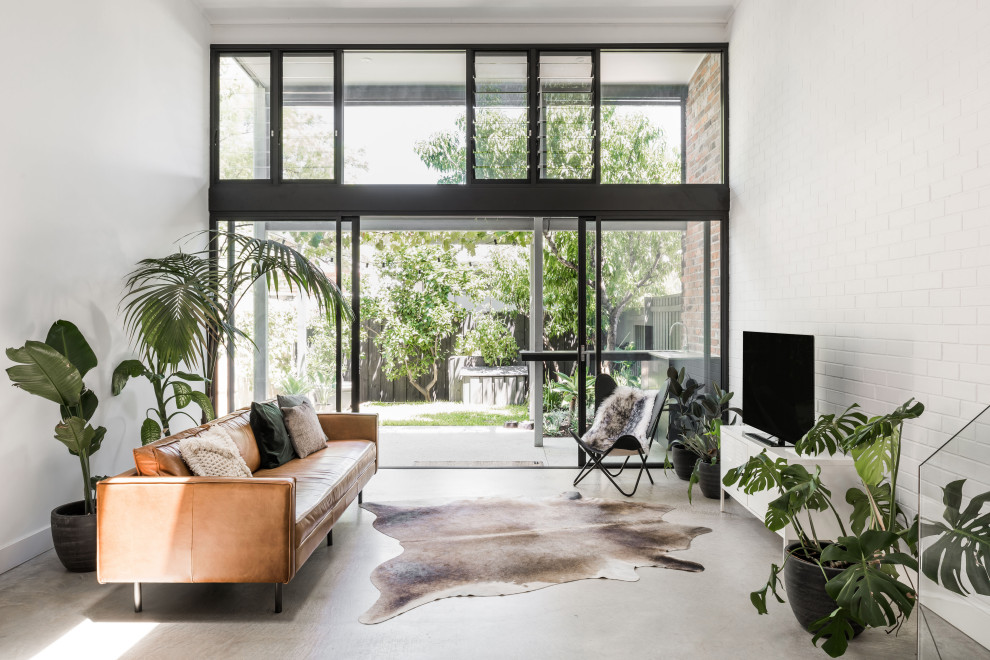 Idee per un soggiorno contemporaneo aperto con pareti bianche, pavimento in cemento, TV autoportante e pareti in mattoni