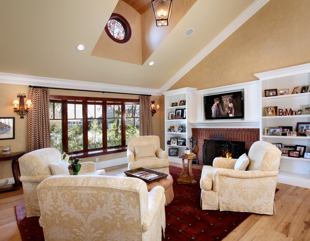 Esempio di un soggiorno chic con sala formale, pareti beige, parquet chiaro, camino classico, cornice del camino in mattoni e TV a parete