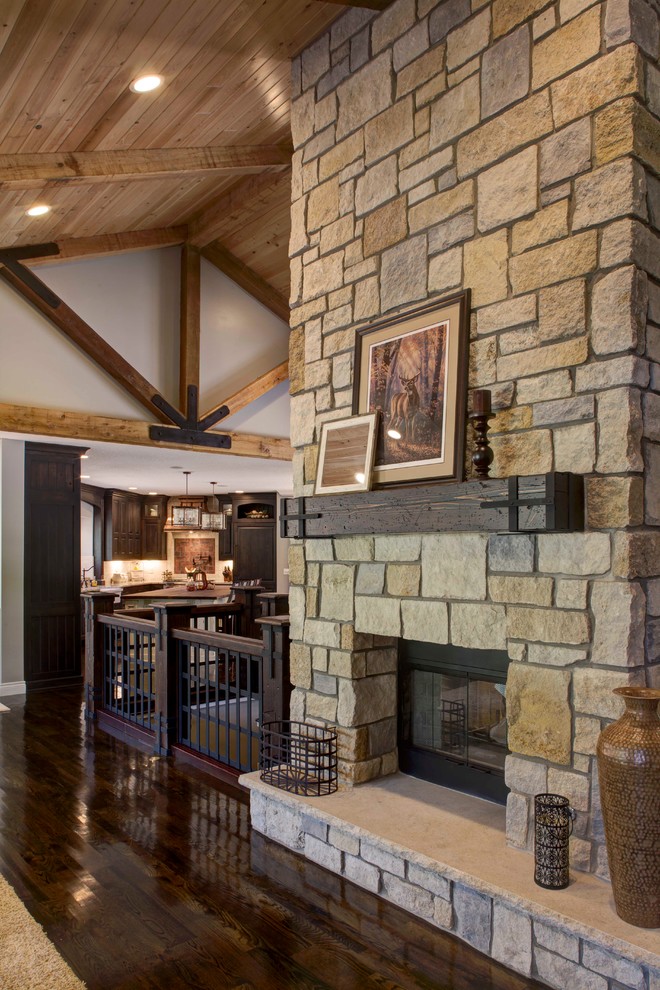 Foto de salón abierto rústico grande sin televisor con paredes grises, suelo de madera oscura, chimenea de doble cara y marco de chimenea de piedra