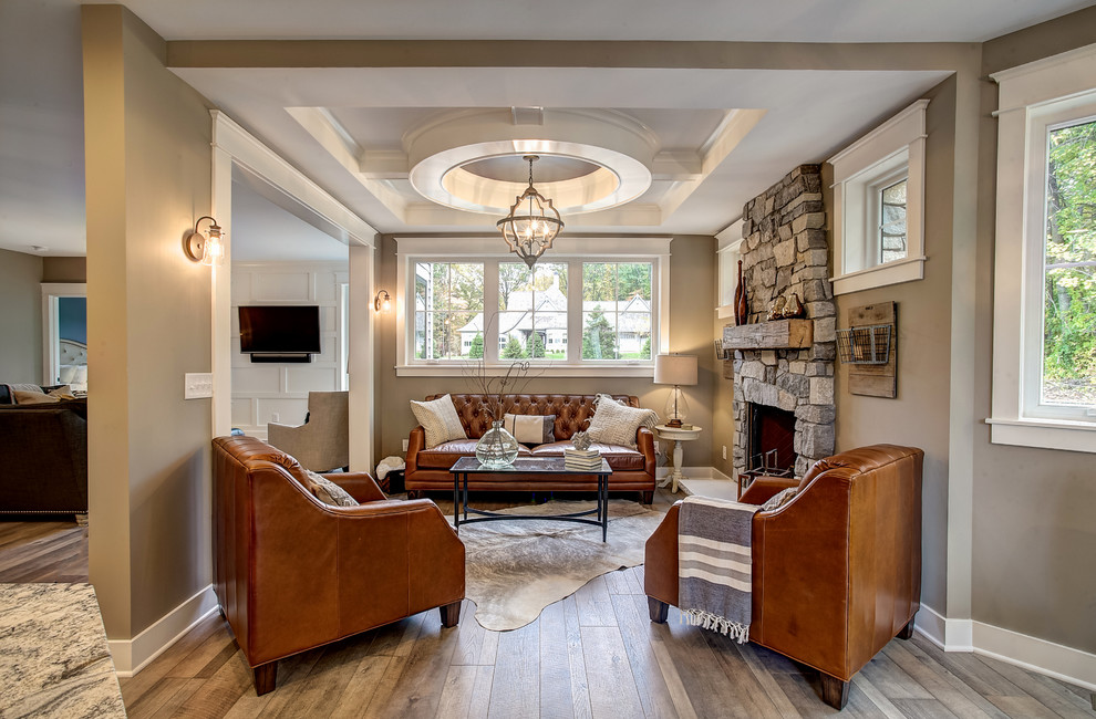 Klassisches Wohnzimmer mit beiger Wandfarbe, hellem Holzboden, Kamin, Kaminumrandung aus Stein und TV-Wand in Grand Rapids