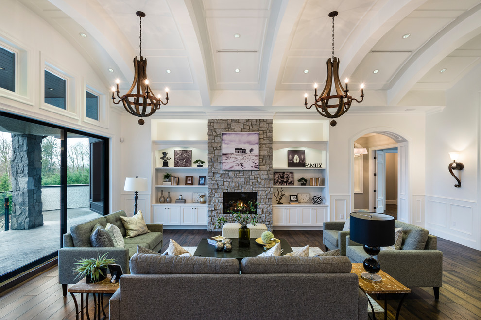 This is an example of an expansive classic formal open plan living room in Vancouver with white walls, a standard fireplace, a stone fireplace surround, no tv, brown floors, dark hardwood flooring and feature lighting.