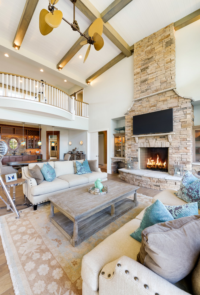 This is an example of a coastal open plan living room in Other with medium hardwood flooring, a stone fireplace surround, a wall mounted tv, a standard fireplace and white walls.