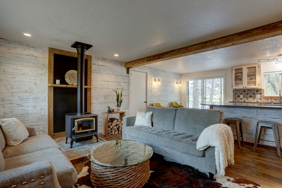 На фото: открытая гостиная комната среднего размера в стиле рустика с белыми стенами, полом из ламината, печью-буржуйкой, фасадом камина из камня и коричневым полом