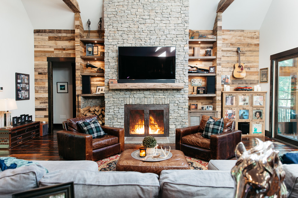 This is an example of a rustic living room in Nashville with white walls, medium hardwood flooring, a standard fireplace, a stone fireplace surround, a wall mounted tv and brown floors.