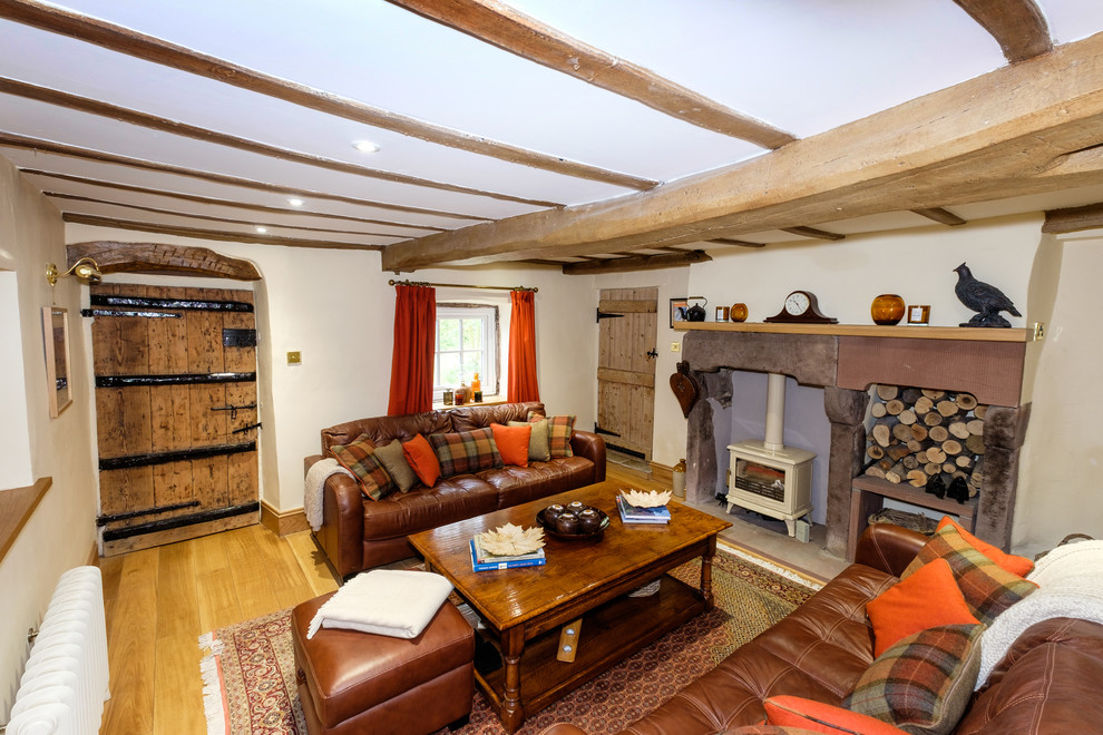 Diseño de salón cerrado rural grande con paredes beige, suelo de madera en tonos medios, estufa de leña y marco de chimenea de piedra