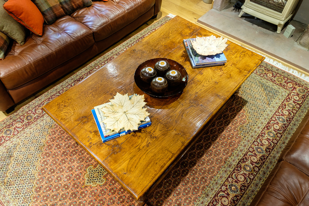 Modelo de salón cerrado rústico grande con paredes beige, suelo de madera en tonos medios, estufa de leña y marco de chimenea de piedra