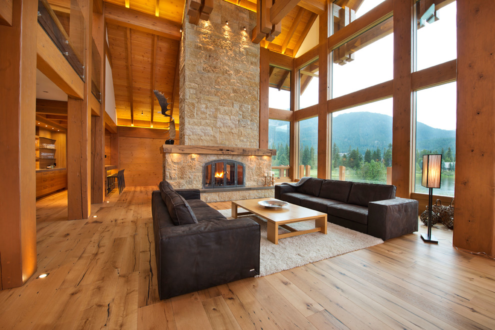 Idée de décoration pour un salon chalet ouvert avec un sol en bois brun, une cheminée standard, un manteau de cheminée en pierre et canapé noir.