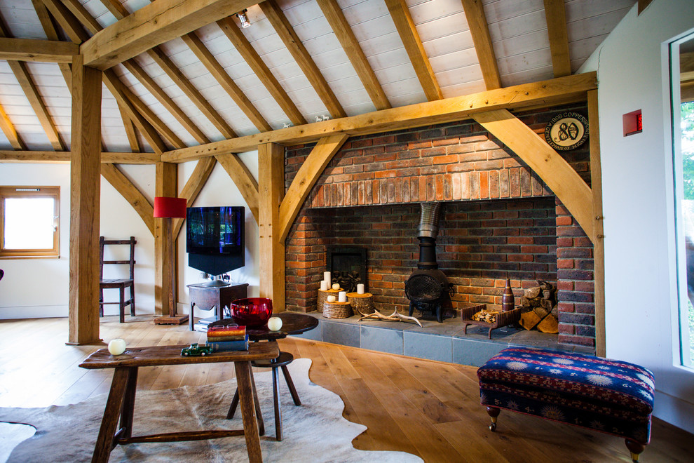 Imagen de salón rural con paredes blancas, suelo de madera en tonos medios, estufa de leña y marco de chimenea de ladrillo