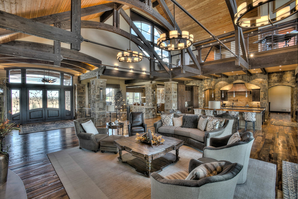 Expansive rustic open plan living room in Denver with a home bar, beige walls, medium hardwood flooring, a standard fireplace, a stone fireplace surround and no tv.