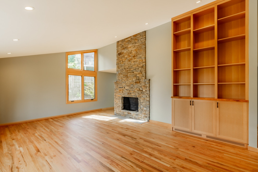 Exemple d'un salon moderne ouvert avec un mur gris, un sol en bois brun, un manteau de cheminée en pierre et un sol orange.