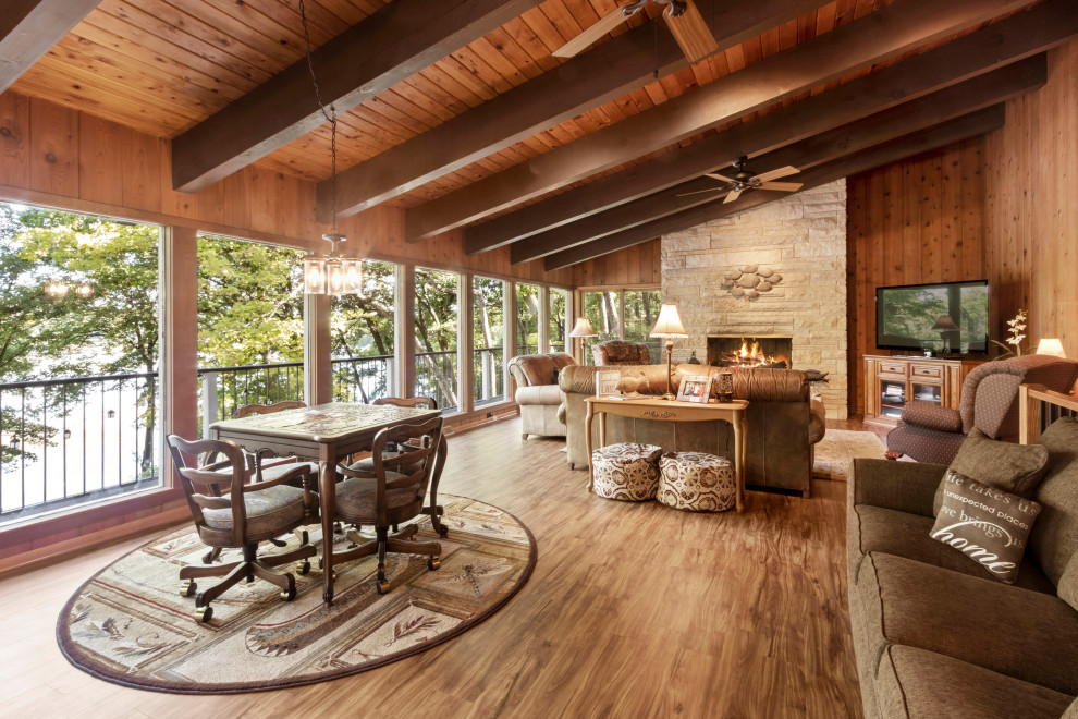 Photo of a large rustic open plan living room in Milwaukee with brown walls, vinyl flooring, a standard fireplace, a stone fireplace surround, a freestanding tv, brown floors, a wood ceiling and wood walls.