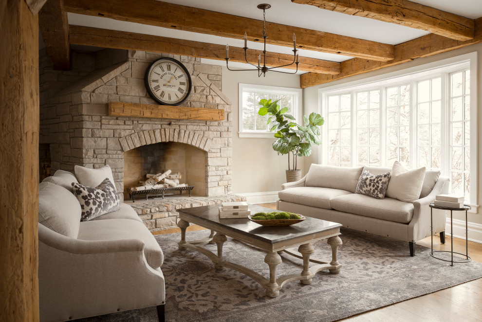 Aménagement d'un salon avec un mur beige, un sol en bois brun, une cheminée standard, un manteau de cheminée en brique, un sol marron et poutres apparentes.