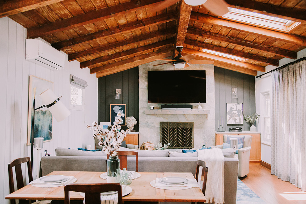 This is an example of a large rustic open plan living room in Los Angeles with a home bar, black walls, bamboo flooring, a standard fireplace, a stone fireplace surround, a wall mounted tv and brown floors.