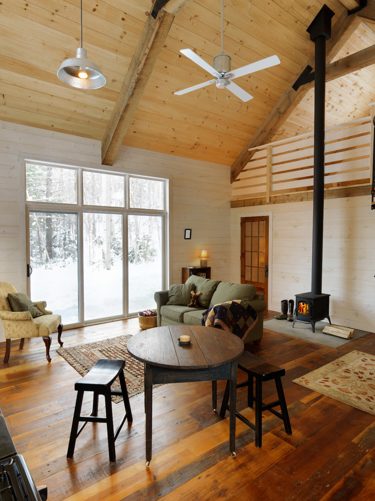 Idée de décoration pour un petit salon chalet avec un poêle à bois, un sol en bois brun, un manteau de cheminée en carrelage et un mur beige.