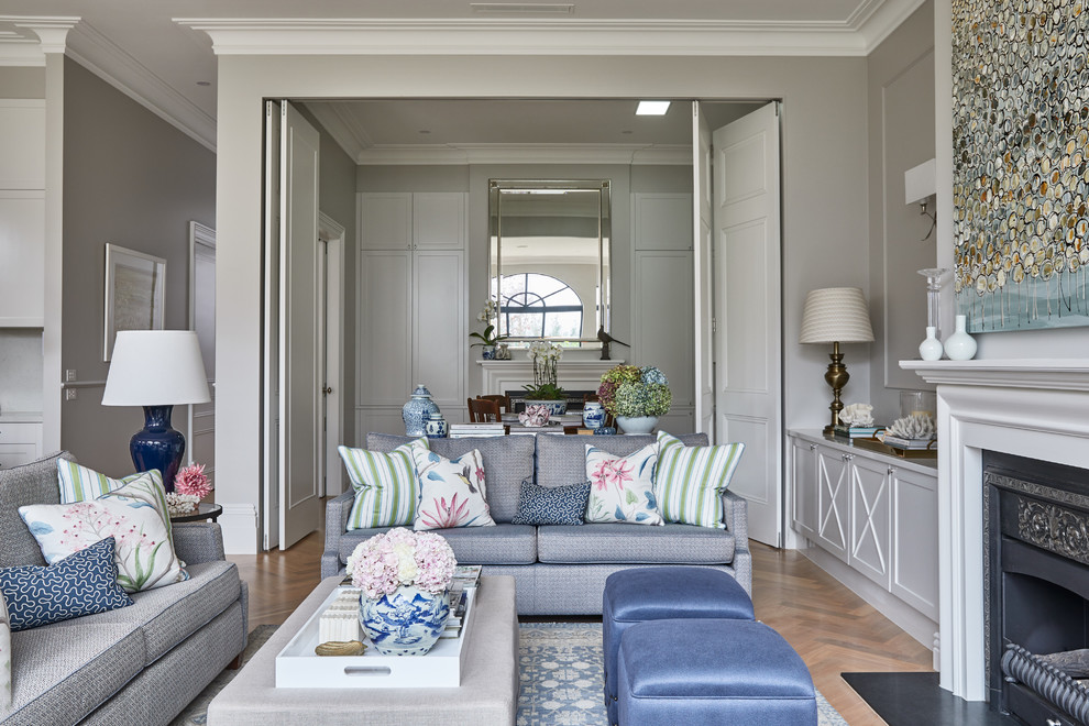 На фото: гостиная комната в классическом стиле с серыми стенами, светлым паркетным полом, стандартным камином, фасадом камина из дерева и мультимедийным центром с