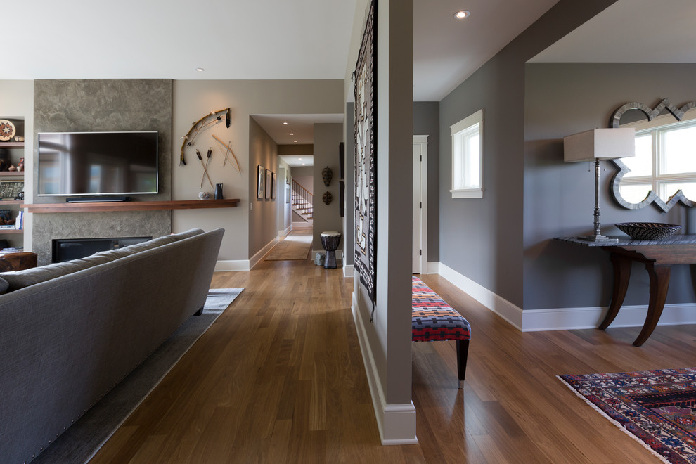 Immagine di un grande soggiorno chic aperto con pareti grigie, cornice del camino in intonaco, TV a parete e pavimento in legno massello medio