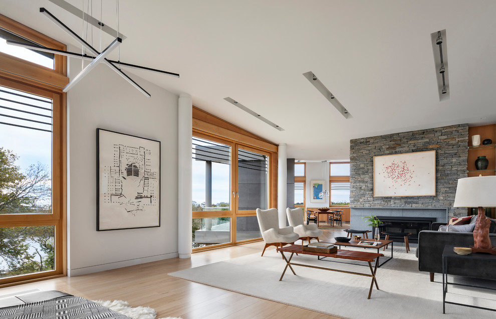 This is an example of a medium sized contemporary open plan living room in New York with white walls, light hardwood flooring, a standard fireplace, a stone fireplace surround and no tv.