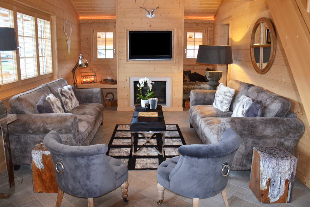 На фото: гостиная комната в современном стиле с бежевыми стенами, фасадом камина из дерева, телевизором на стене, полом из сланца и стандартным камином