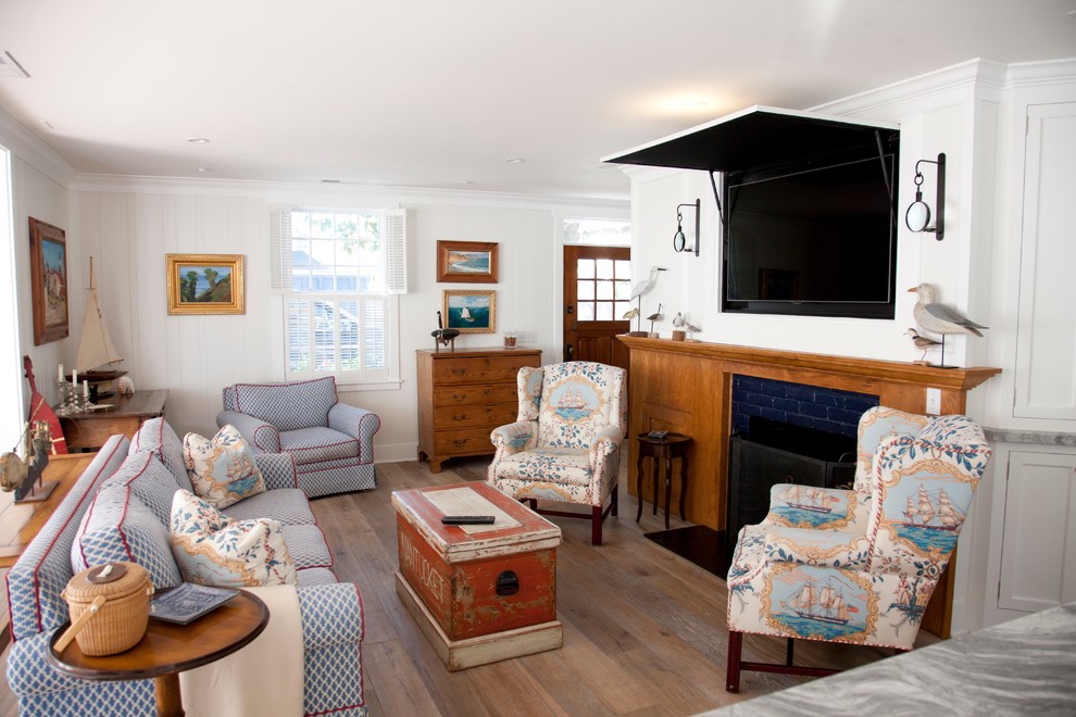 Foto på ett maritimt vardagsrum, med vita väggar, en dold TV, ett finrum, mellanmörkt trägolv, en standard öppen spis och en spiselkrans i trä