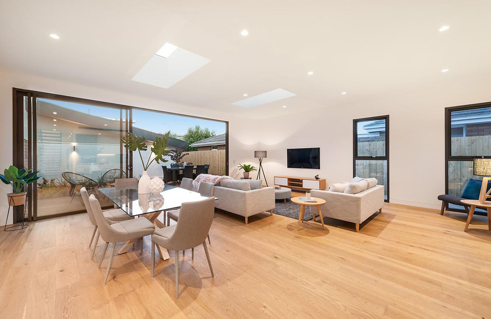 Diseño de salón para visitas abierto actual grande con paredes blancas, suelo de madera clara, televisor colgado en la pared y suelo beige