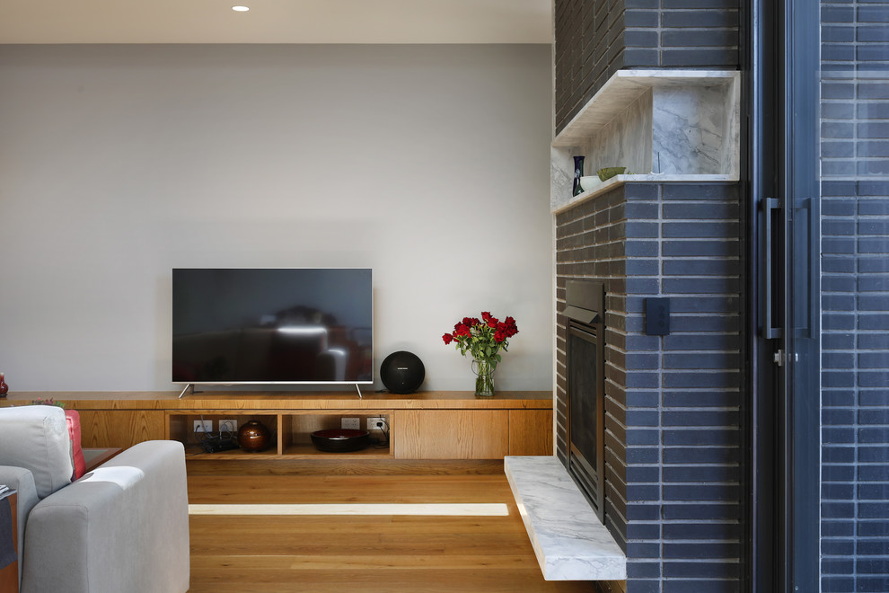 Example of a large trendy formal and open concept light wood floor and beige floor living room design in Melbourne with white walls, a standard fireplace, a brick fireplace and a tv stand