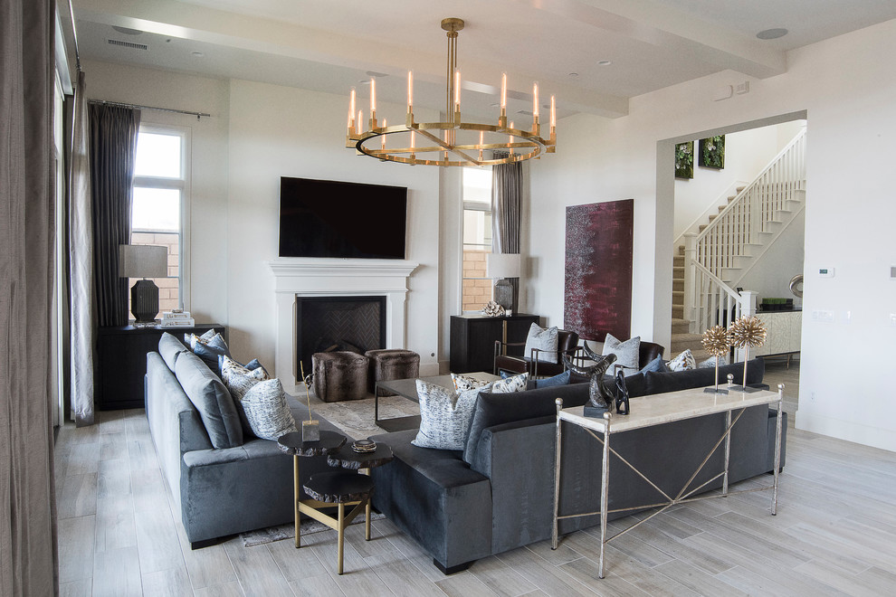 This is an example of a medium sized contemporary formal open plan living room in Orange County with white walls, light hardwood flooring, a standard fireplace, a wooden fireplace surround, a wall mounted tv and grey floors.