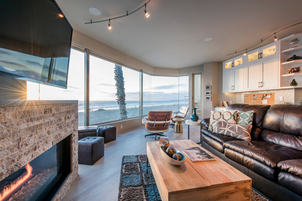 サンディエゴにある高級な広いビーチスタイルのおしゃれなLDK (ベージュの壁、淡色無垢フローリング、標準型暖炉、石材の暖炉まわり、壁掛け型テレビ) の写真