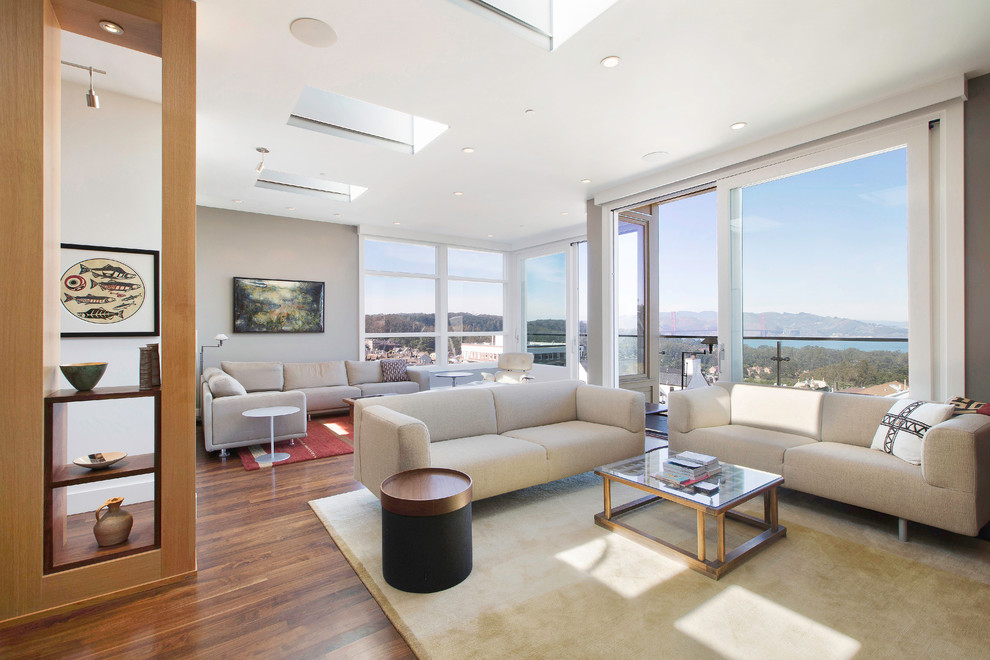 Cette image montre un grand salon design ouvert avec un mur gris, un sol en bois brun et un téléviseur encastré.